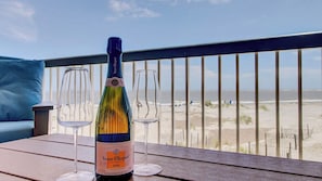 Une bouteille de champagne Veuve Clicquot sur une table en bois, avec deux verres vides, donnant sur une plage.