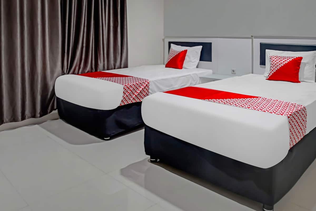 Two beds with white and red bedding, a dark headboard, and a curtain in the background.