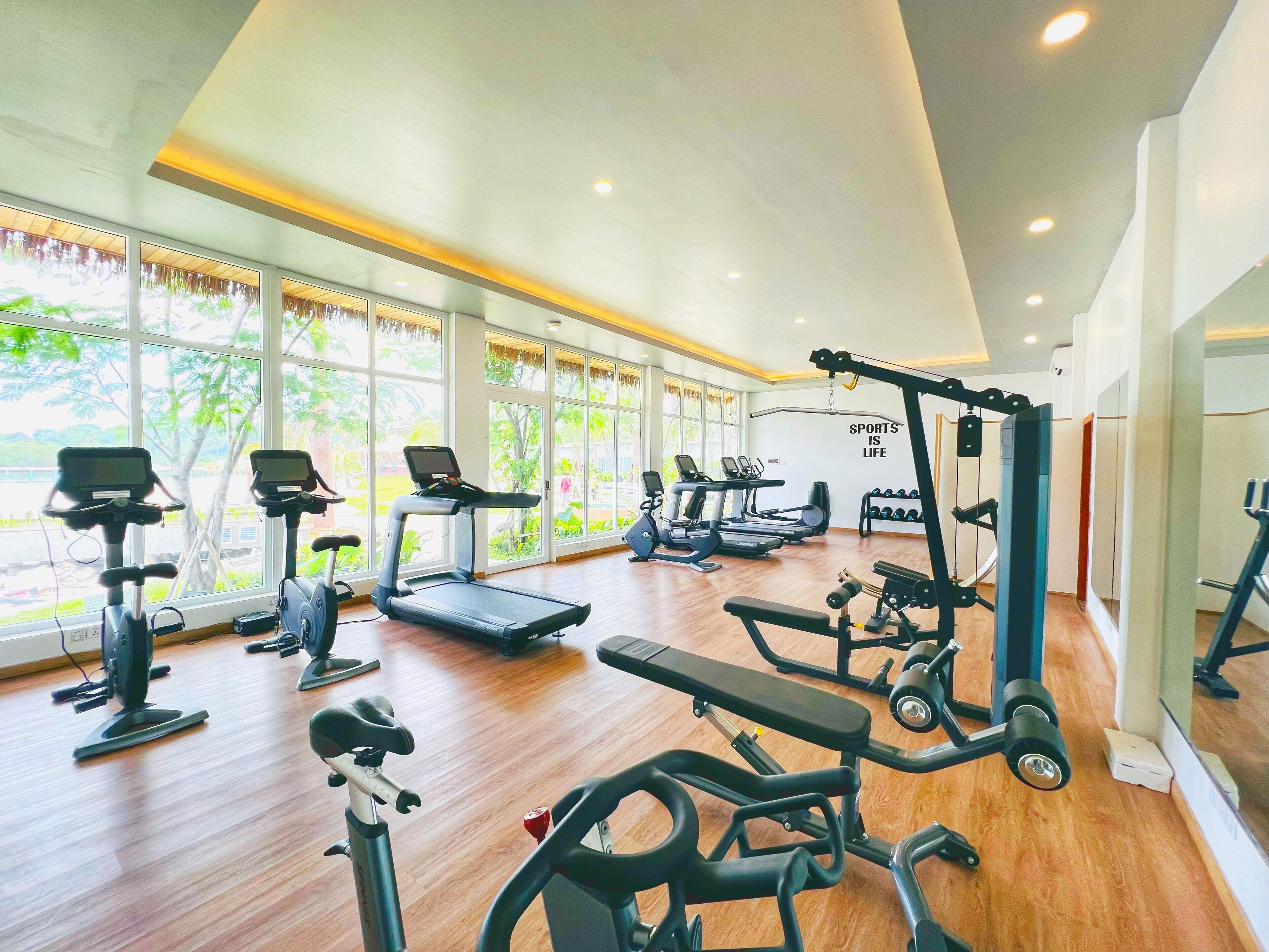 A gym with various exercise equipment, large windows, and a motivational quote on the wall.