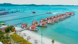 Un complejo turístico frente al mar con bungalows sobre el agua, unidos a una playa de arena por pasarelas.