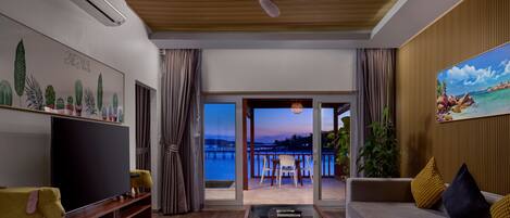A modern living room with a flat-screen TV, a ceiling fan, a sofa, and a view of a waterfront.