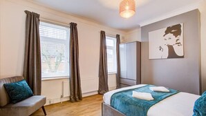 A bedroom with a bed, a chair, a wardrobe, and a painting on the wall.