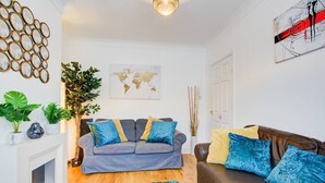 A modern living room with a grey sofa, a brown leather sofa, and a blue shag rug. There is a world map on the wall and a plant in the corner.