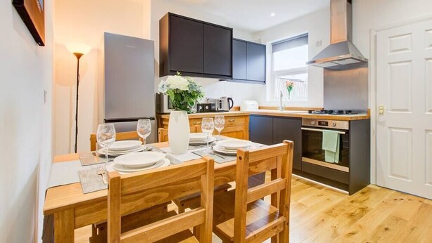 A compact kitchen with dark cabinets, a built-in oven, and a dining area with wooden chairs and a table set for two.