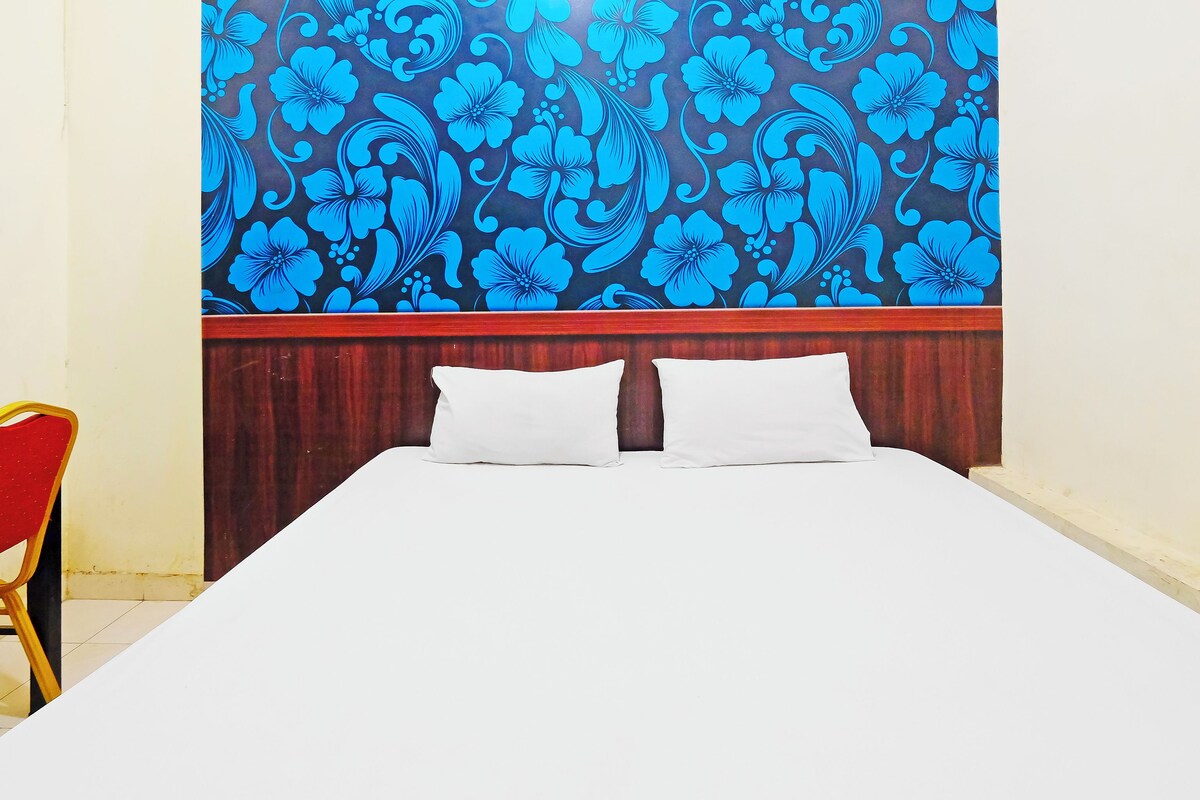 A hotel room with a bed, two pillows, a wooden headboard, and a red chair.