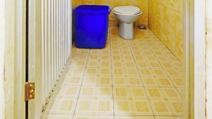 A small bathroom with yellow tiles, a toilet, and a blue trash bin.