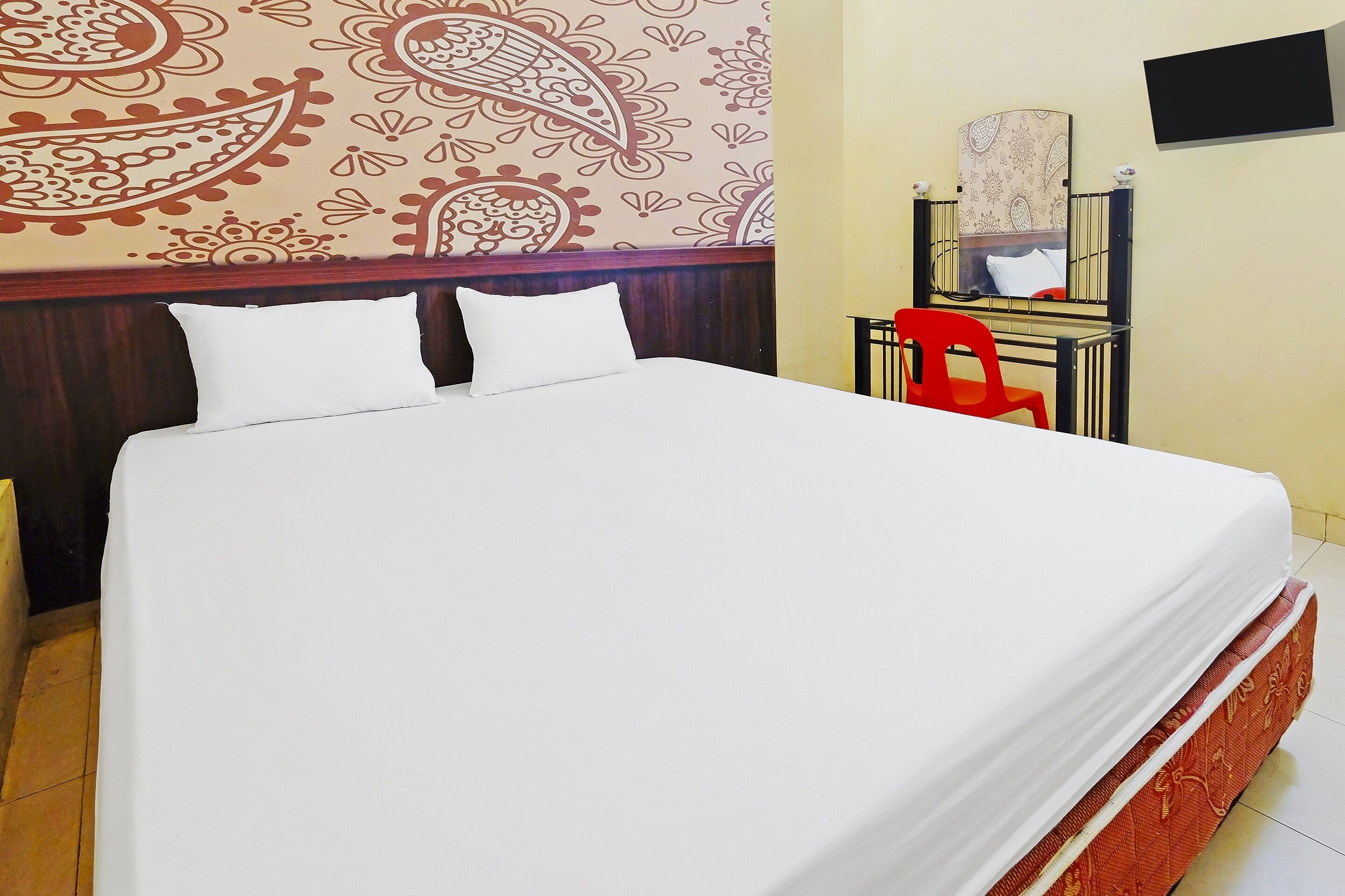 Una cama bien hecha con ropa blanca, una silla roja y un espejo en la pared.