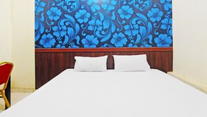A hotel room with a bed, two pillows, a wooden headboard, and a floral-patterned wall.