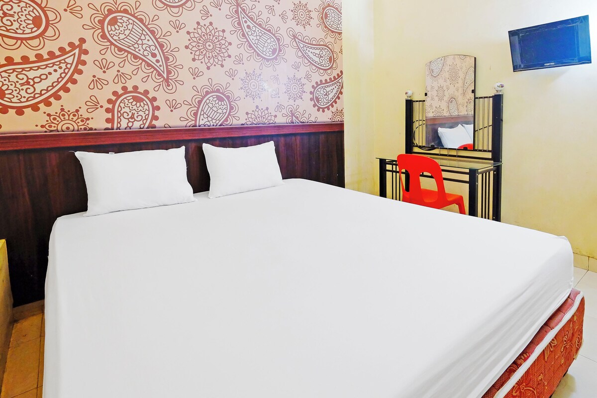 A hotel room with a large bed, a red chair, a TV, and a patterned wall.