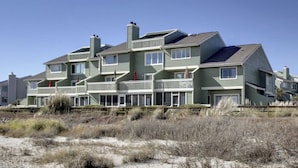 A multi-story residential building with balconies, a sandy beach in the foreground, and clear skies.