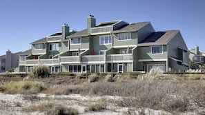 Un immeuble résidentiel à plusieurs étages doté de balcons, une plage de sable au premier plan et un ciel dégagé.