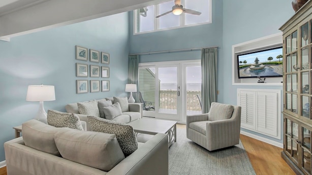 A living room with a sofa, armchair, coffee table, and a television on a wall.
