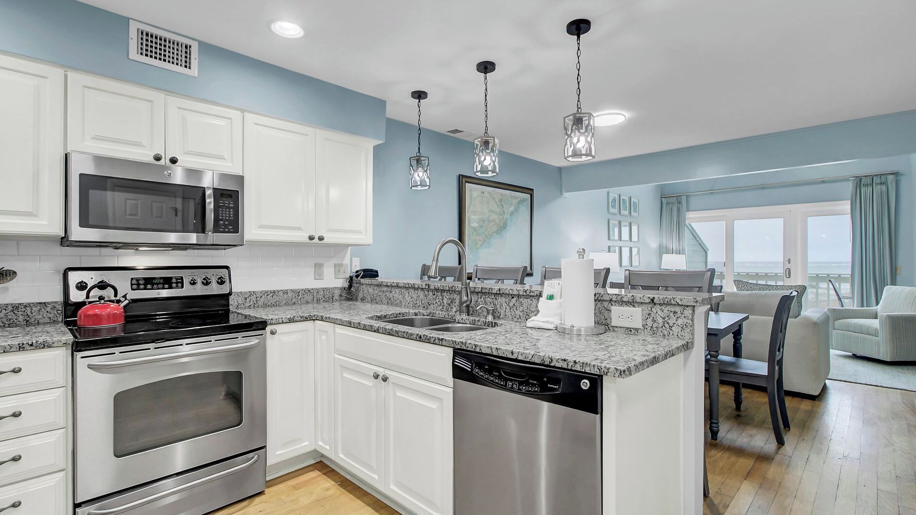 A modern kitchen with white cabinets, stainless steel appliances, granite countertops, and pendant lighting.