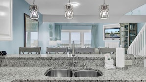 A kitchen with granite countertops, stainless steel sink, and pendant lighting.