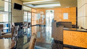 A hotel lobby with a reception desk, seating area, and glass doors leading to the outside. - OYO 3691 Apartment Saladin Mansion (Depok)