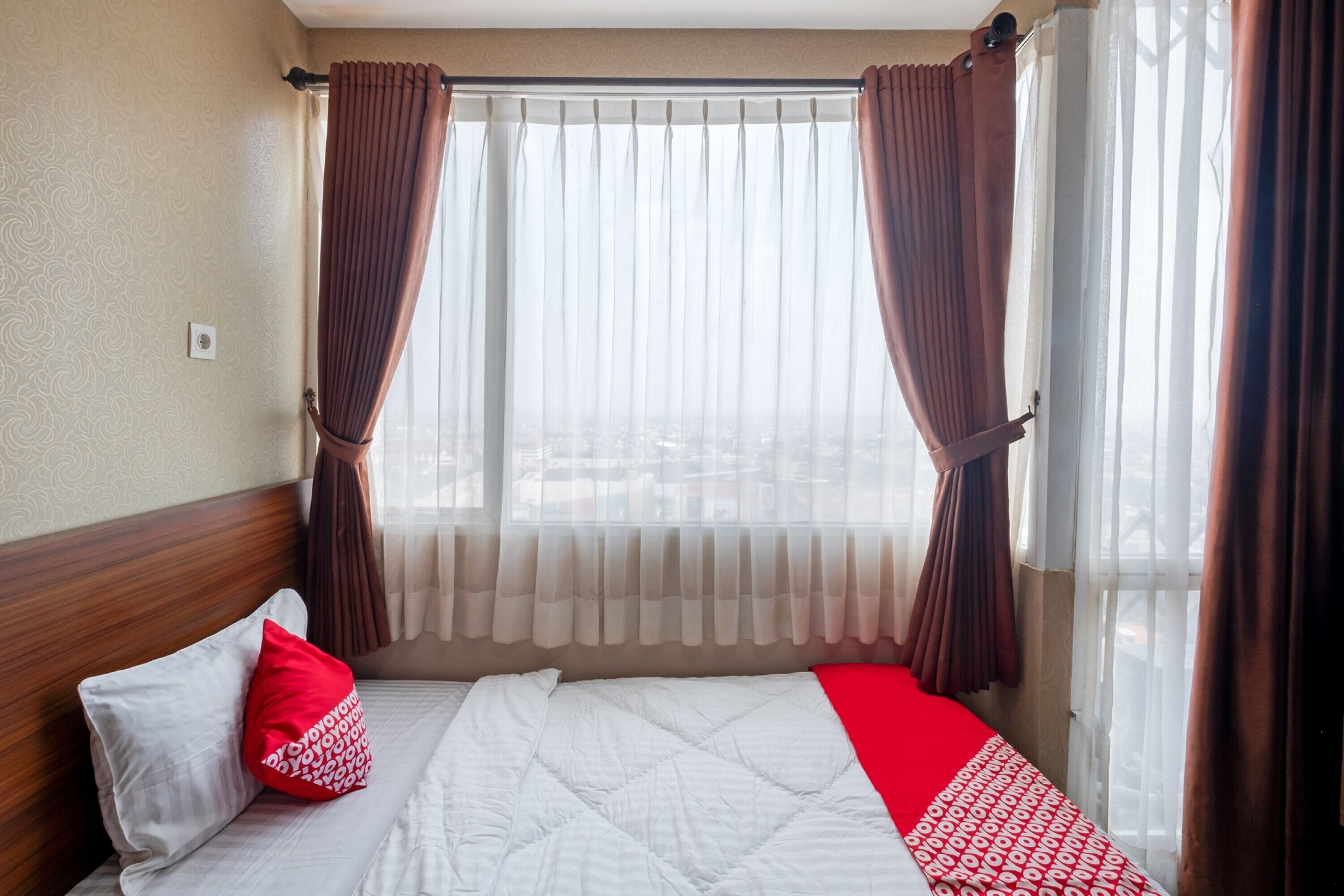 A hotel room with a bed, a window with curtains, and a view of the outside.