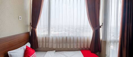 A hotel room with a bed, a window with curtains, and a view of the outside.