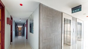 A modern hotel corridor with a polished floor, wooden panel wall, and an exit sign. - OYO 3691 Apartment Saladin Mansion (Depok)