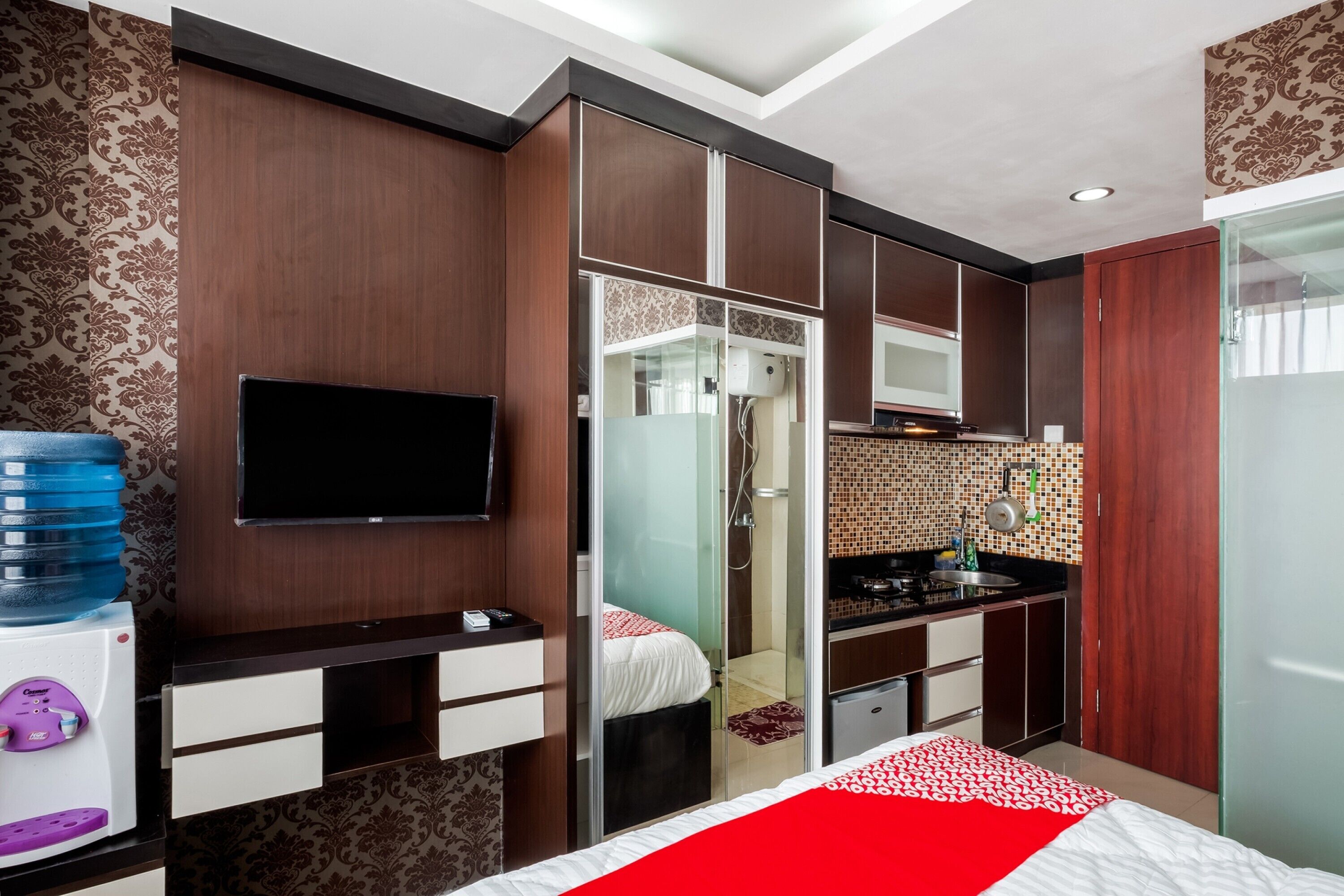 A hotel room with a bed, a TV, a wardrobe, a bathroom with a shower, and a kitchenette.