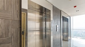 A modern elevator with a metallic finish, adjacent to a wooden panel wall and a glass door. - OYO 3691 Apartment Saladin Mansion (Depok)