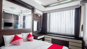 A modern hotel room with a large bed, a vanity with a mirror, a window with curtains, and a built-in air conditioning unit. - OYO 3691 Apartment Saladin Mansion (Depok)