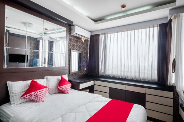 A modern hotel room with a large bed, a vanity with a mirror, a window with curtains, and a built-in air conditioning unit.