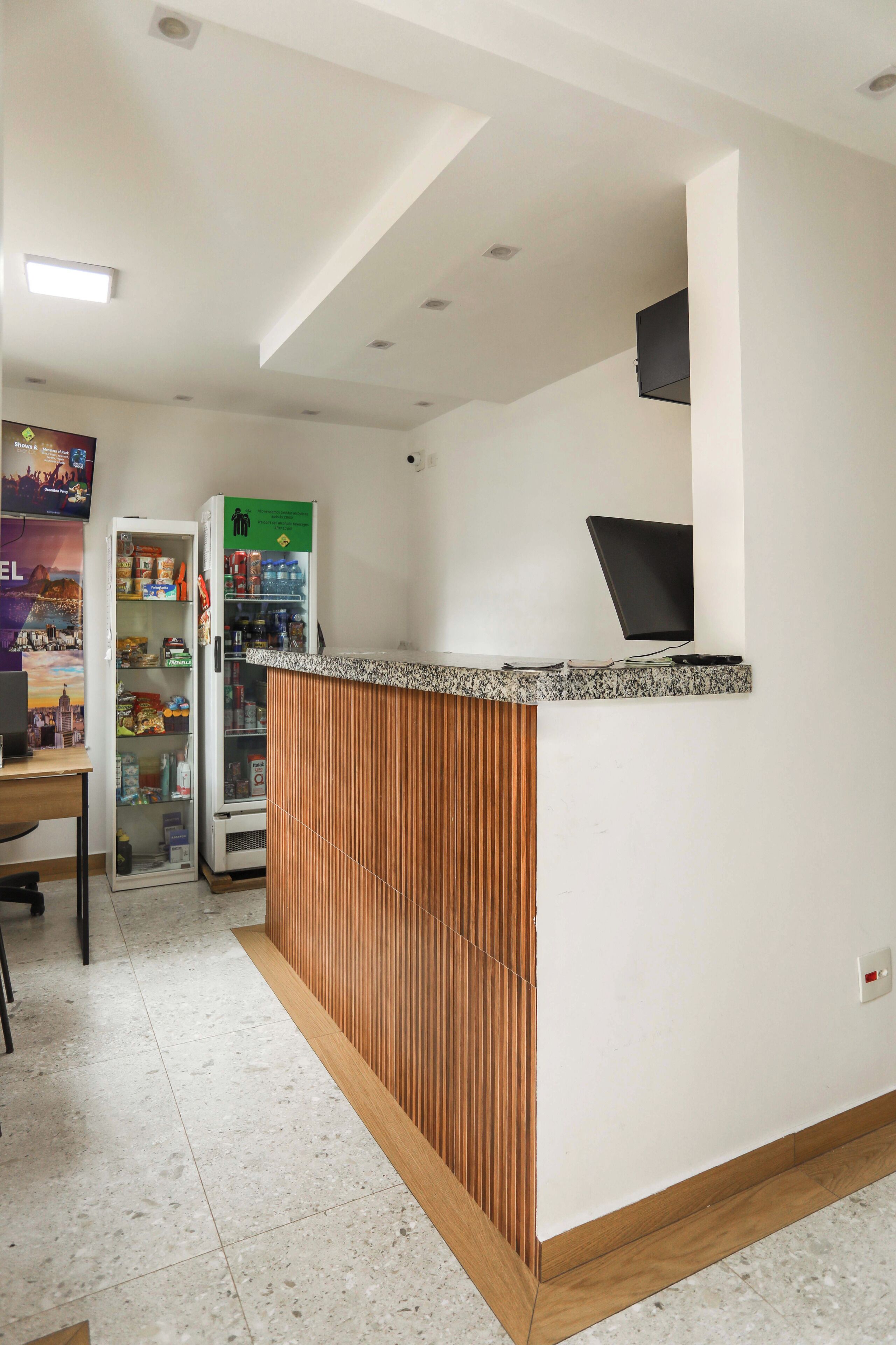 A reception area with a wooden counter, a refrigerator stocked with beverages, and a wall-mounted television.