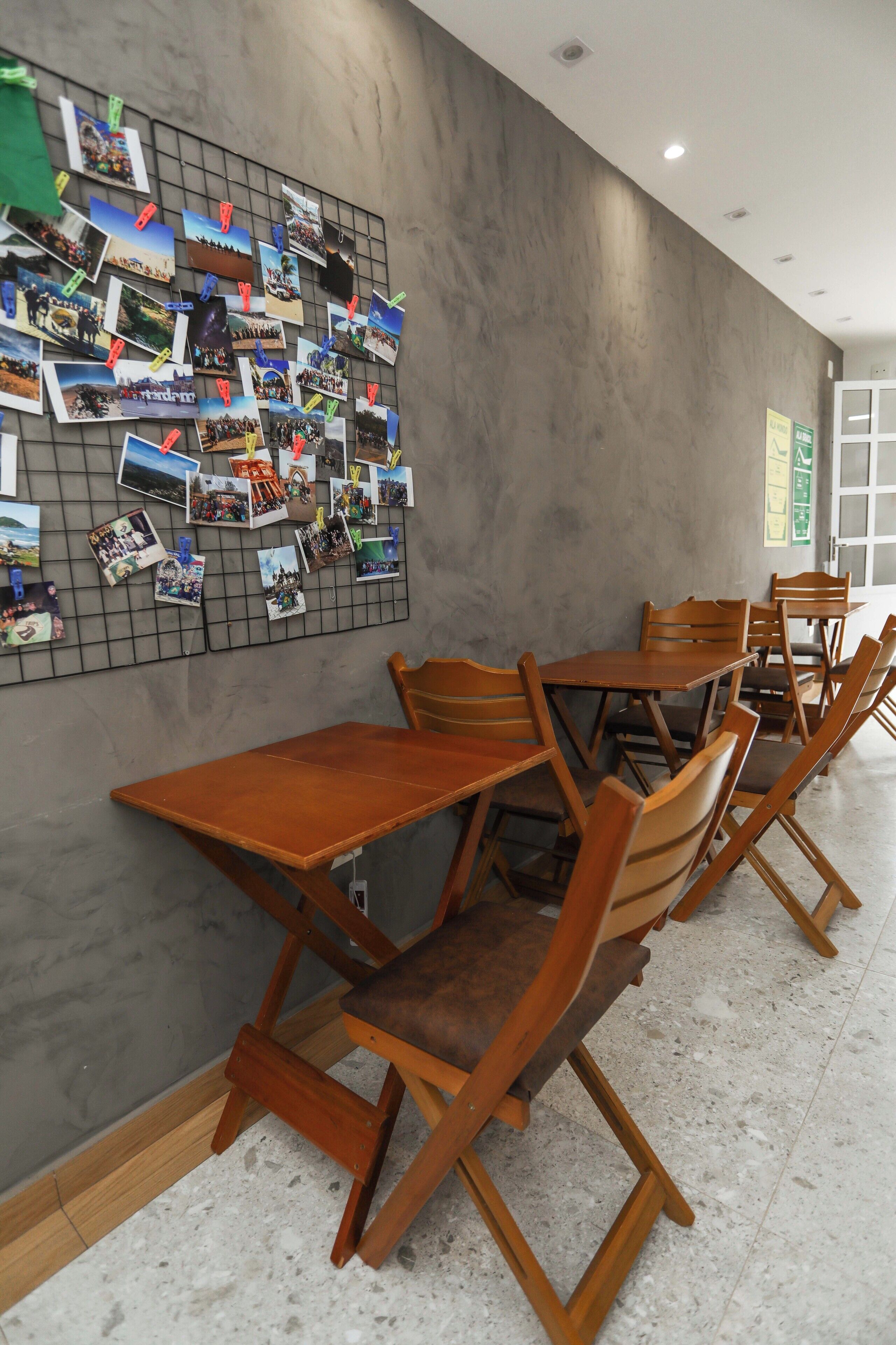 Un espace repas avec des tables et des chaises en bois, un tableau d’affichage où sont accrochées des photos, et un mur sobre.