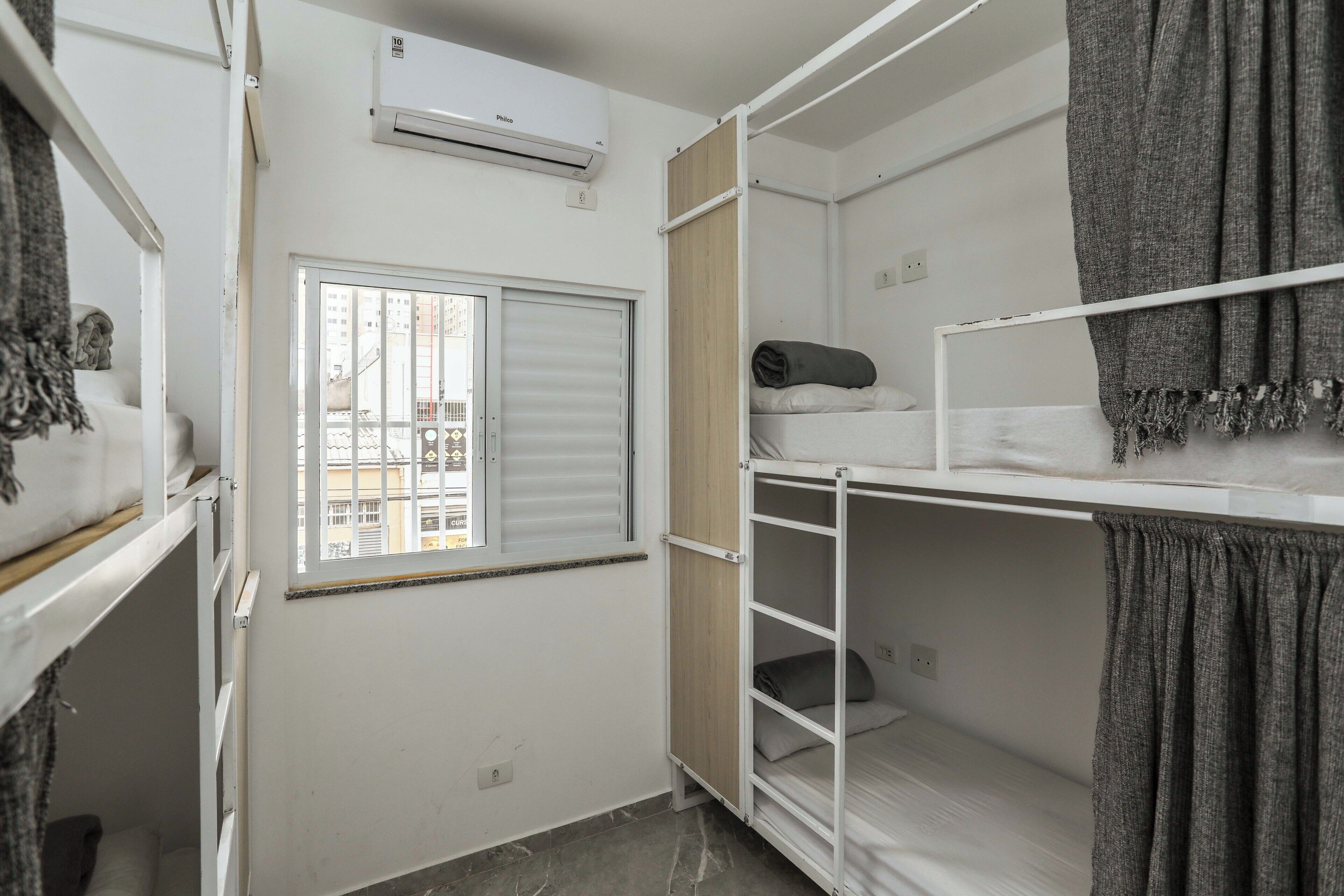 A compact room with bunk beds, a window with blinds, an air conditioner, and a small window view.