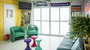 Una habitación con dos sillones verdes, un taburete púrpura y uno rosa, un sofá azul y un ventanal con vistas al exterior.