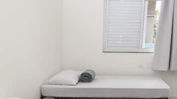 A small, clean room with two beds, one with a mattress and pillows, and a rolled-up towel on the floor.