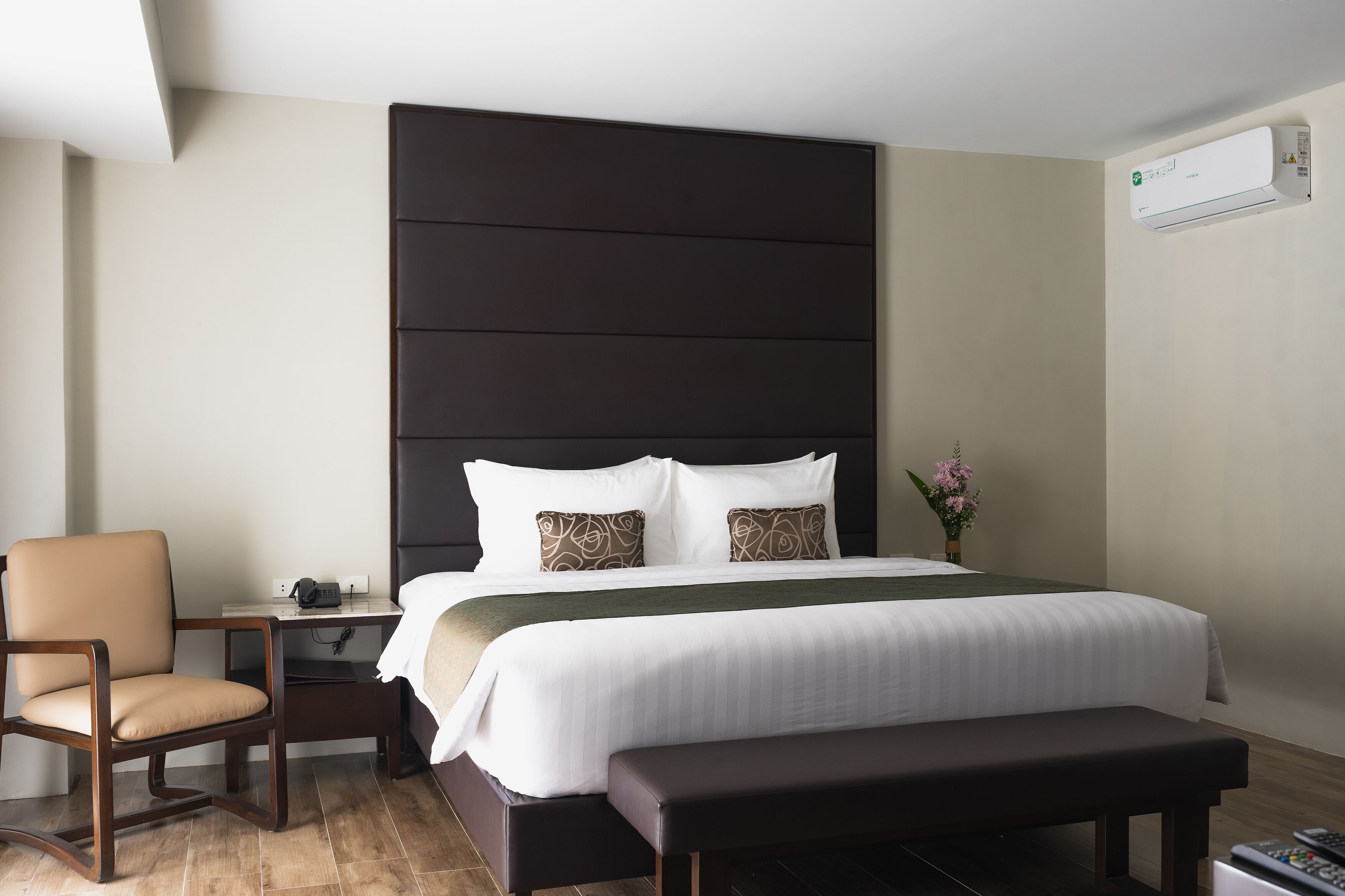 Una habitación de hotel con una cama grande, una mesita de noche, una silla y un banco.