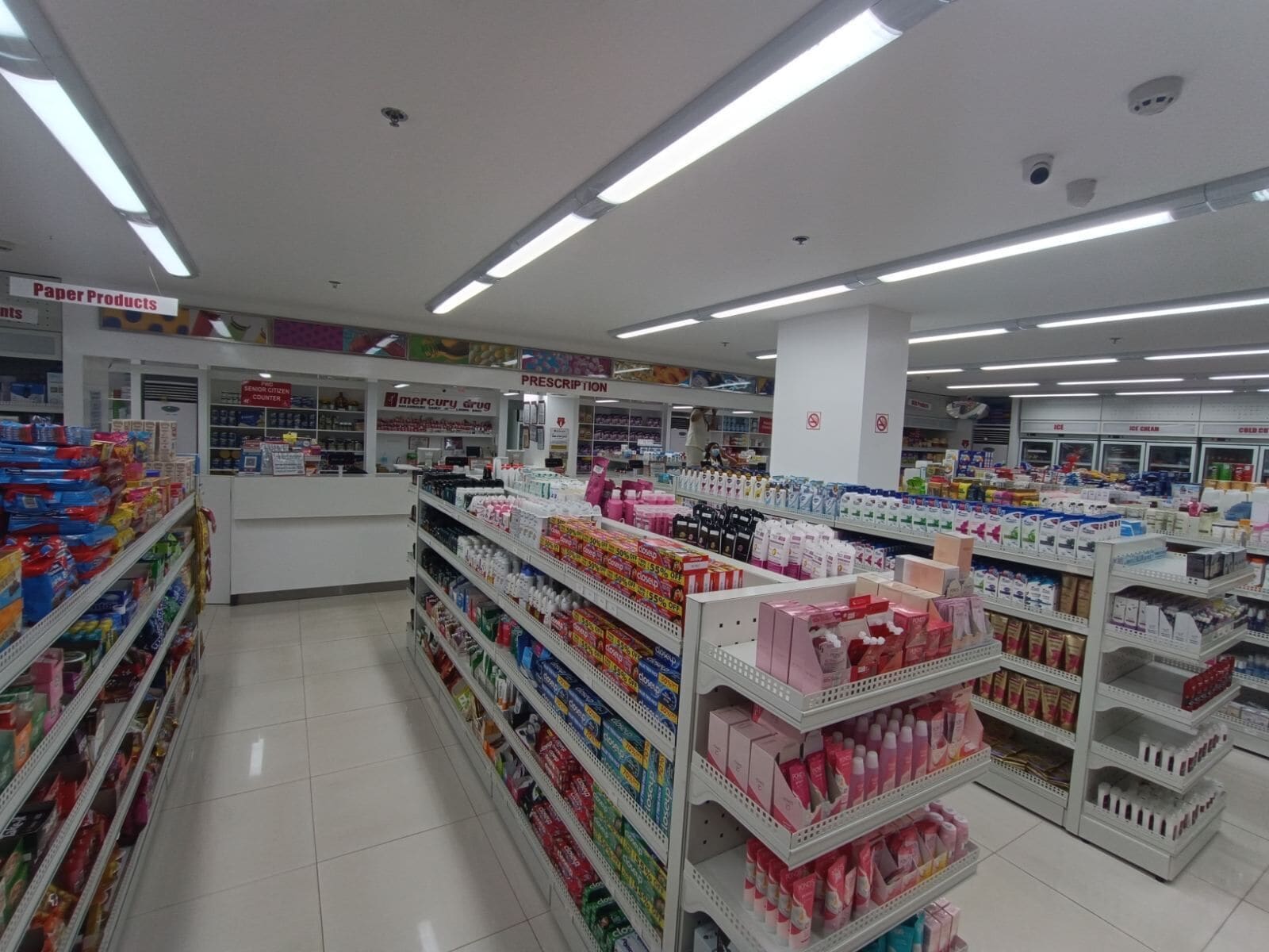 A pharmacy aisle with shelves stocked with various products, including paper products and prescription items.