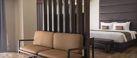 A modern hotel room with a brown leather sofa, a round table, and a large bed with a dark headboard.