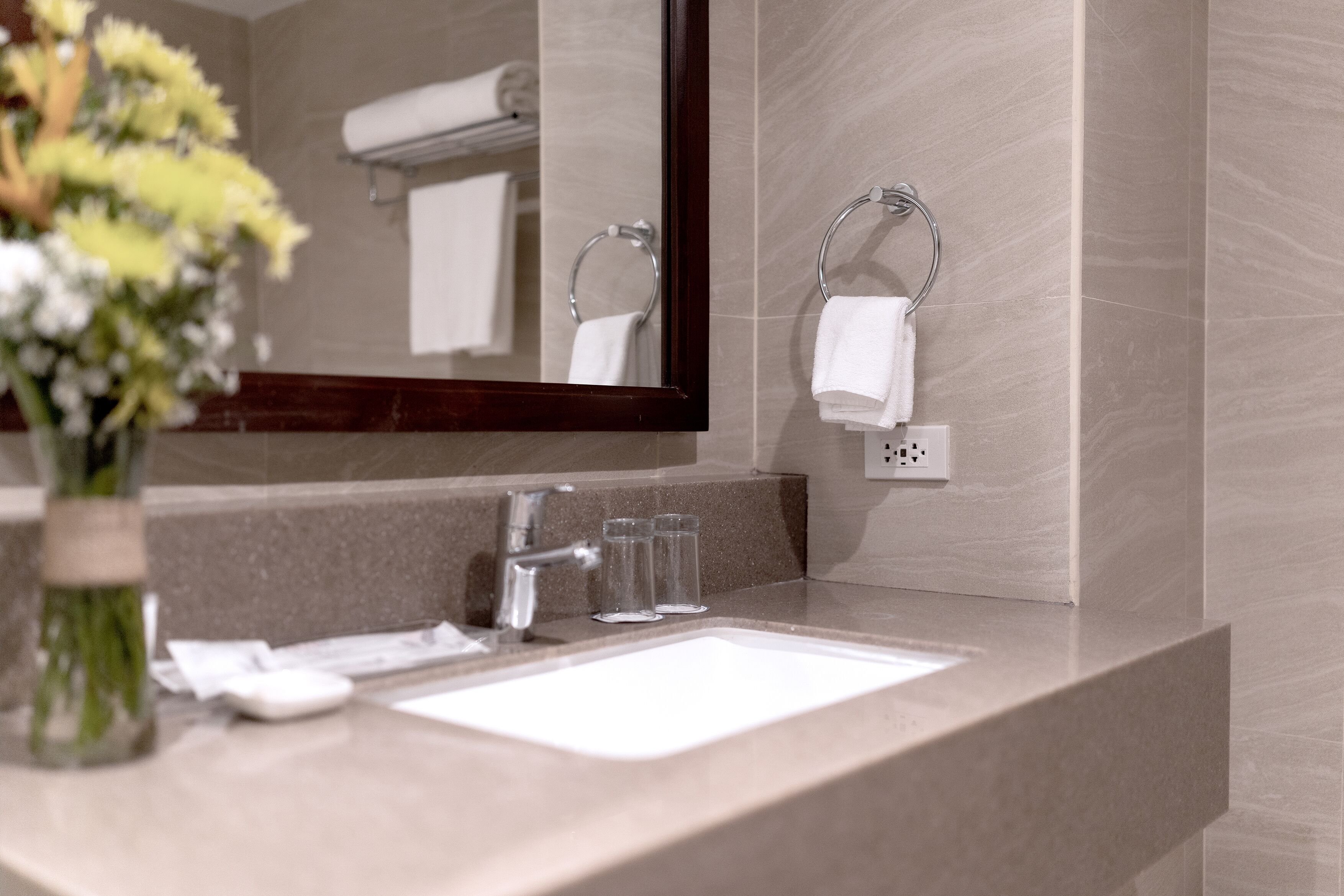 Un baño con lavamanos, espejo, toallero y un jarrón de flores.