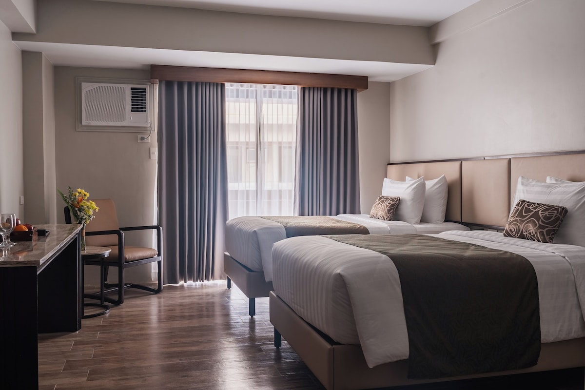 Une chambre d’hôtel avec deux lits, un bureau, une chaise et une fenêtre avec des rideaux.
