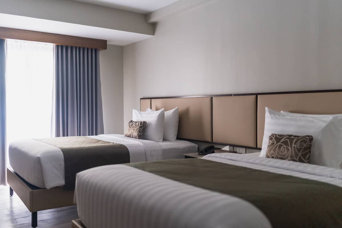 Ein Hotelzimmer mit zwei Betten, einem Nachttisch und einem Fenster mit Vorhängen.