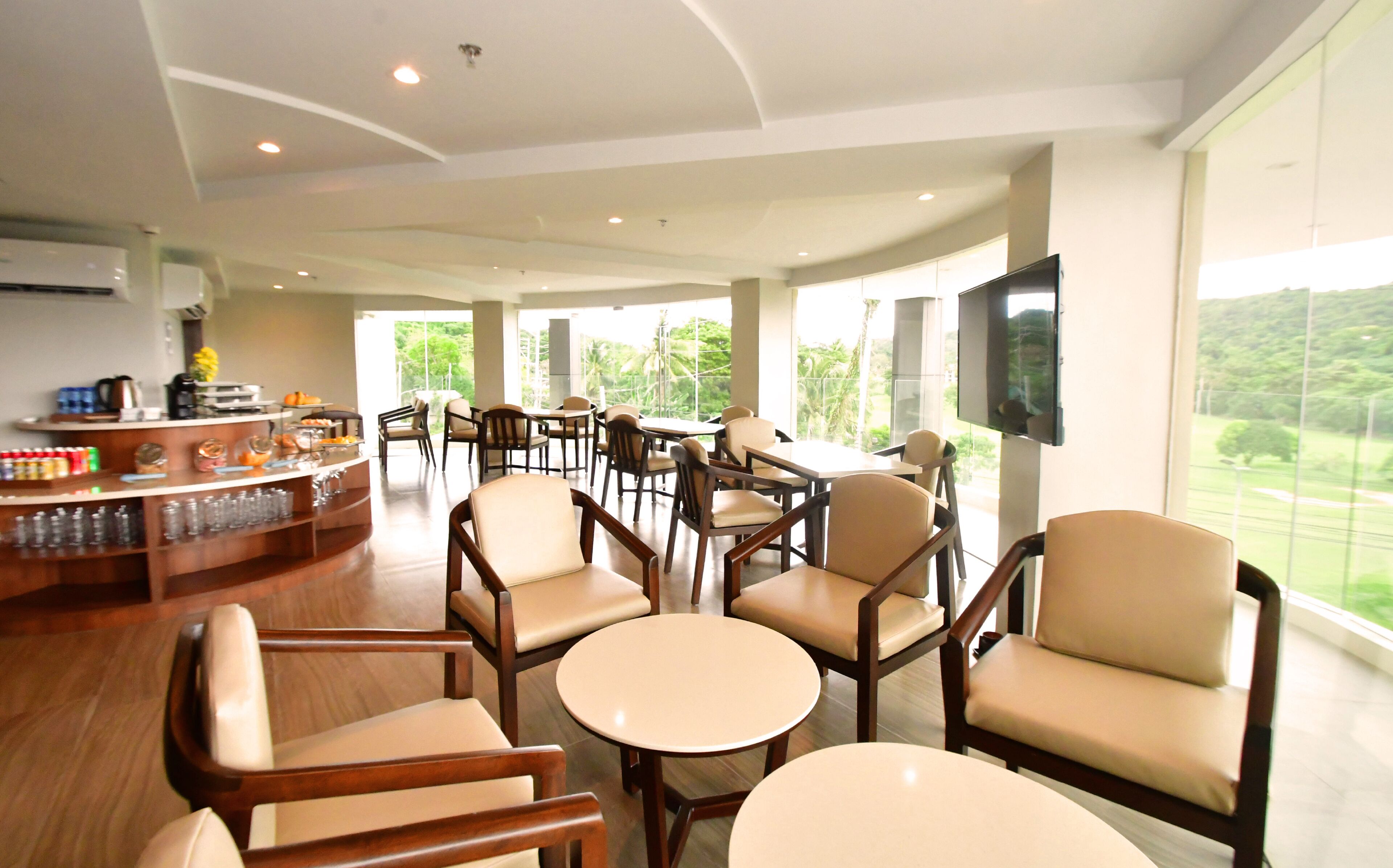 A spacious indoor area with multiple seating arrangements, a bar area, and a large window offering a view of greenery.