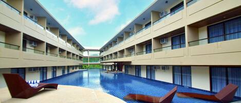 A modern hotel with a central swimming pool, multiple balconies, and a clear sky.