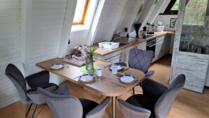 Comedor con una mesa de madera, cuatro sillas grises y una cocina al fondo.