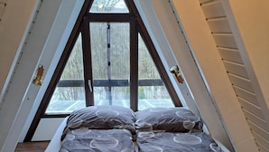 Una cama en una habitación triangular en el ático con un ventanal grande.