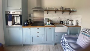 A compact kitchen with a built-in oven, a stainless steel range hood, a sink, and a wooden countertop. There are cabinets with drawers and a small shelf above the sink.