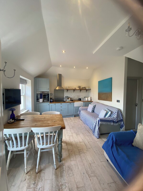 A modern kitchen with white cabinets, a wooden dining table, and a blue sofa.