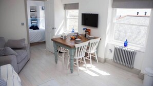 A compact living space with a dining area, a sofa, a TV mounted on the wall, and a window with a view of the roof.