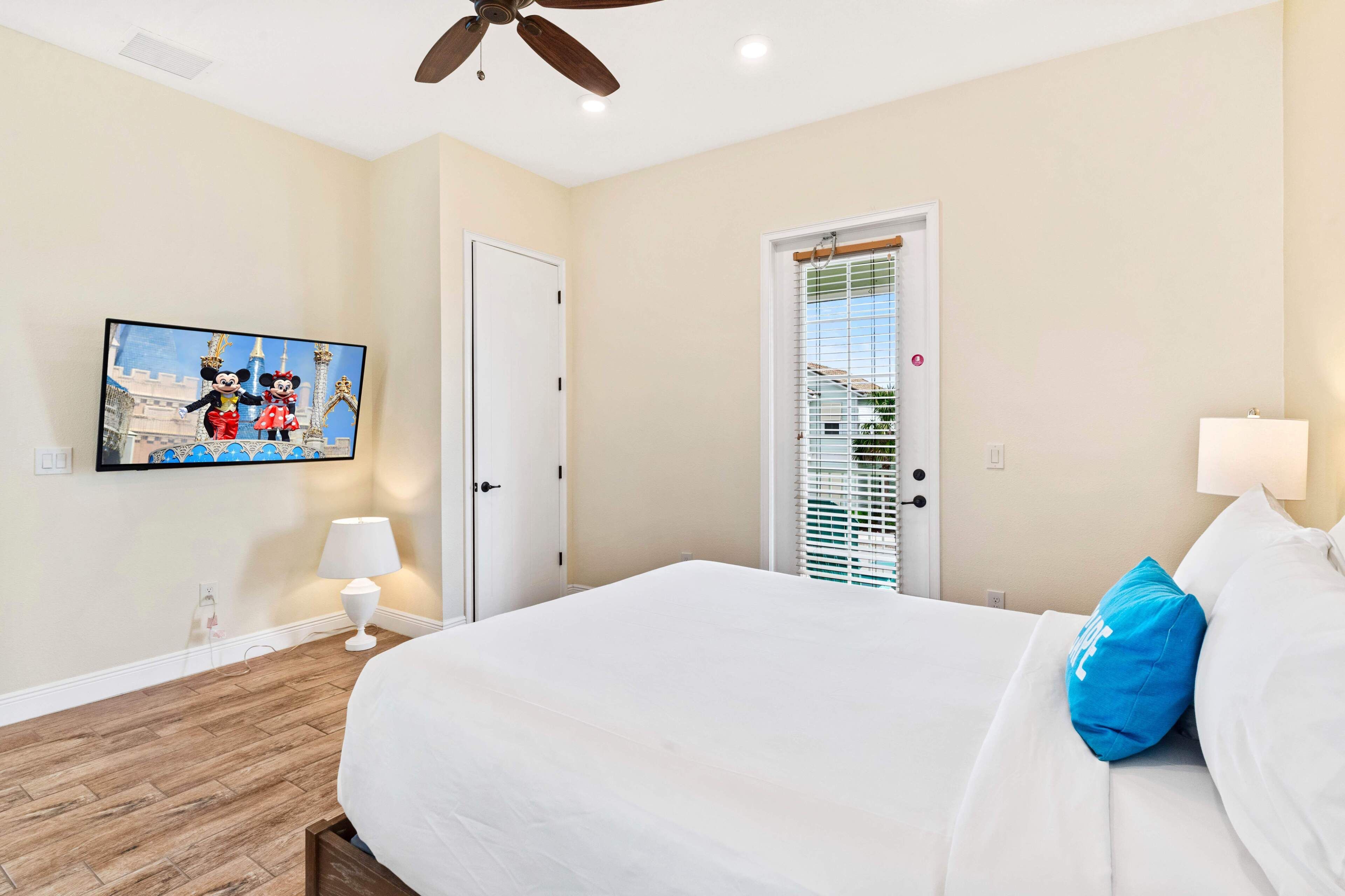 A hotel room with a bed, a ceiling fan, a door, and a window with blinds.