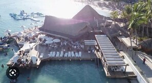 Un resort frente a la playa con piscina, sillones de descanso y bar.