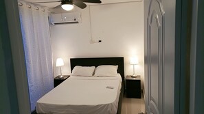 Una habitación de hotel con cama, dos lámparas de noche, ventilador de techo y aire acondicionado.