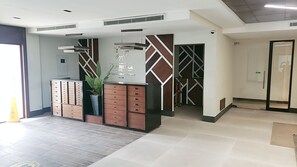 Zona de recepción con diseño moderno, que incluye un mostrador, una planta en maceta y una pared con patrones geométricos.