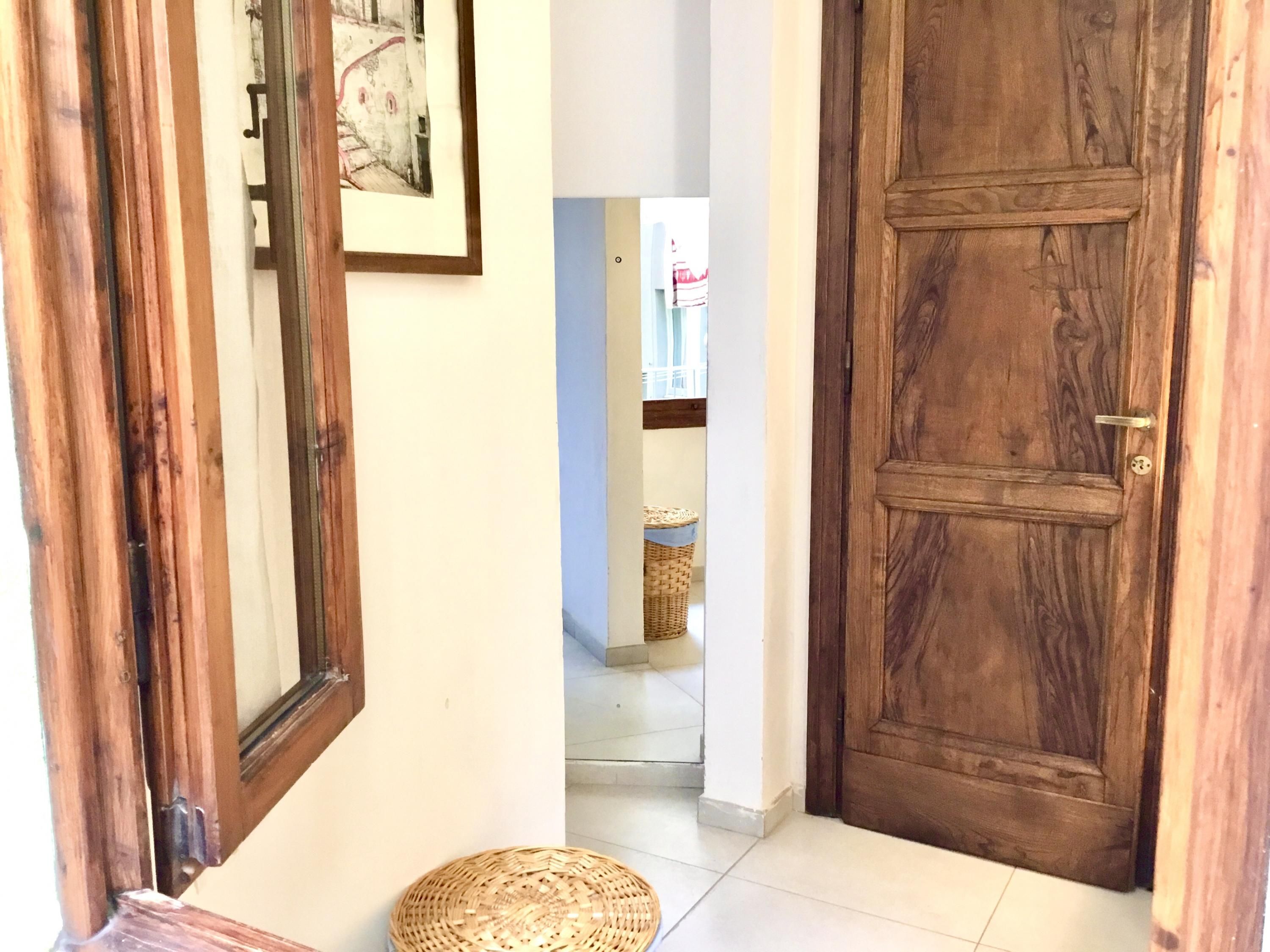 A wooden door with a brass handle, a woven basket on the floor, and a framed picture on the wall.