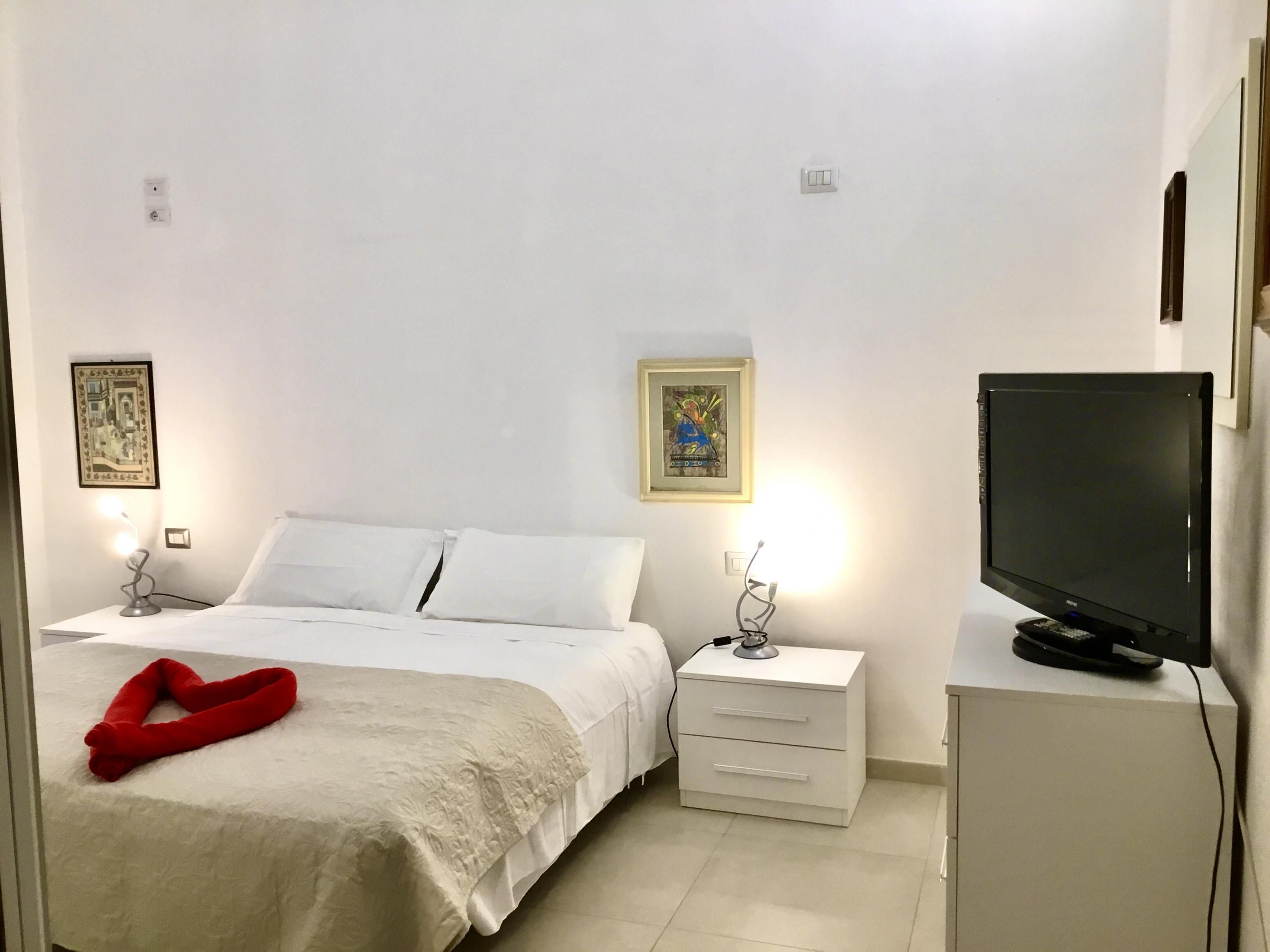 A hotel room with a bed, bedside tables, a TV, and artwork on the walls.